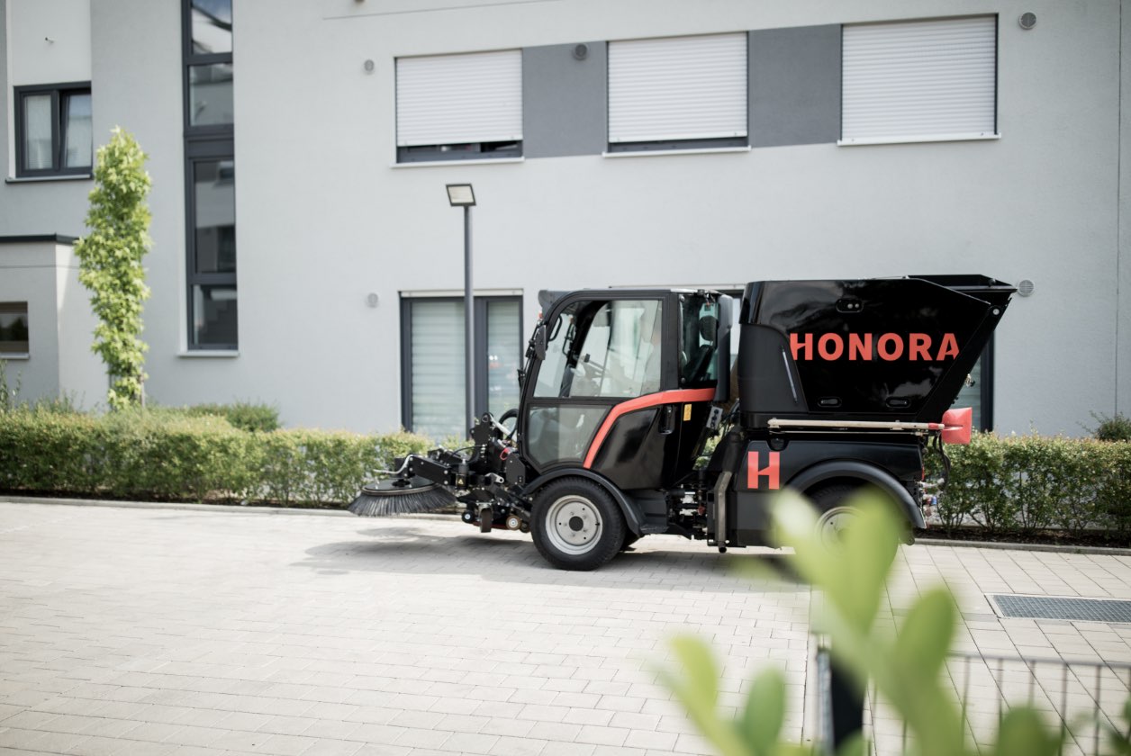 Eine Kehrmaschine der Honora parkt vor einem Mehrfamilienhaus