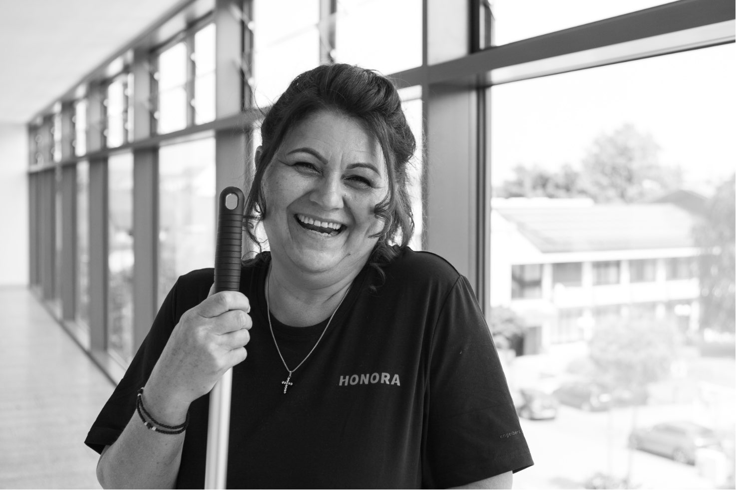Eine Mitarbeiterin des Reinigungsservice der Honora lächelt mit Wischmobb in der Hand in die Kamera