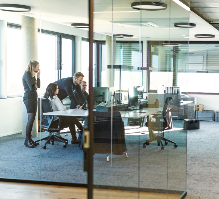 Blick in ein Büro der Honora - Mitarbeiter schauen gemeinam auf einen Monitor und kümmern sich um die Immobilienverwaltung ihrer Kunden