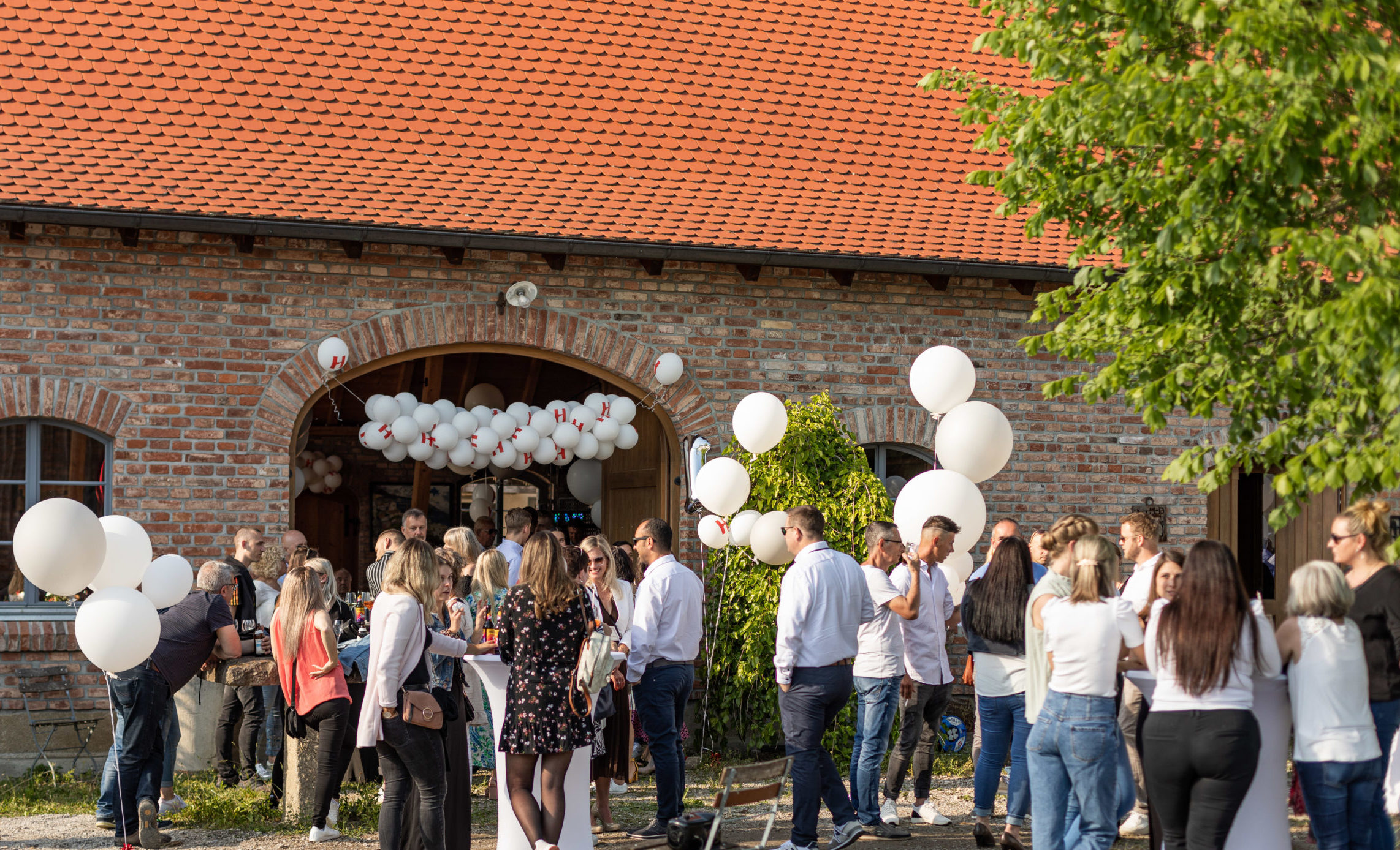 Mitarbeite der Honora feiern an Stehtischen im Freien stehend das 10-jährige Jubiläum der Hausverwaltung.